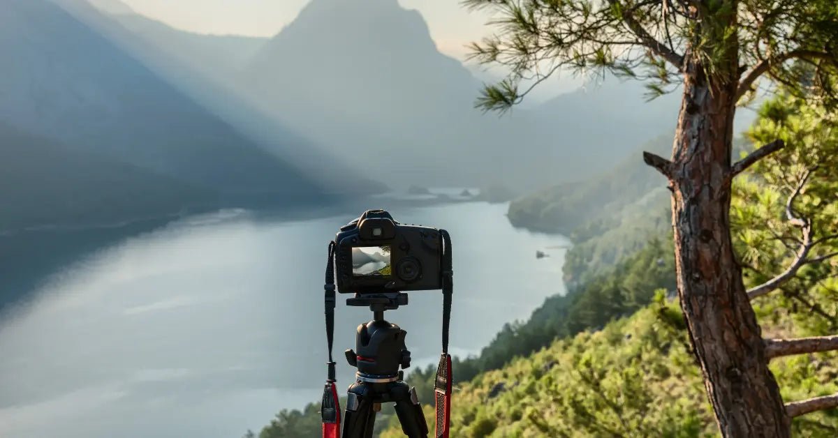 Camera on tripod perched on a forest overlook capturing a serene lake view with distant mountains and fog, showcasing advanced landscape photography.